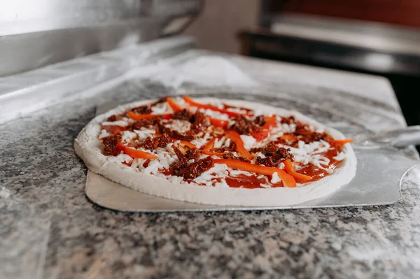 Preparing traditional italian pizza. Chef holds long irob shovel for pizza, baking dough with pasta and cheese in a professional oven.