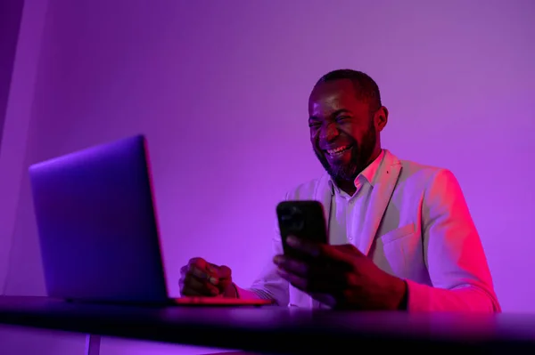 the man is happy at the computer. a dark-skinned man works in the evening office.