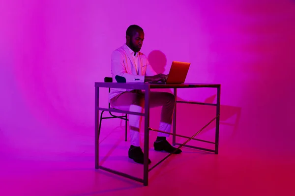 A black programmer works using a laptop computer. the man works at night. office with neon lighting