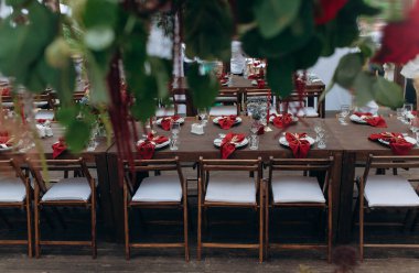 outdoor wedding. long banquet tables, on the tables are flower arrangements, candles, plates with napkins, glasses and cutlery in autumn style
