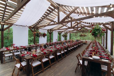 A large, long, decorated, wooden table and chairs, with dishes, flowers, candles. Pavilion in the forest in nature. Wedding banquet. banquet in nature