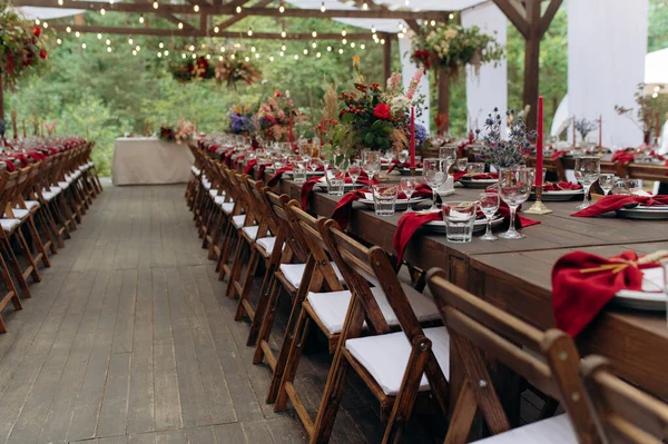 A large, long, decorated, wooden table and chairs, with dishes, flowers, candles. Pavilion in the forest in nature. Wedding banquet. banquet in nature
