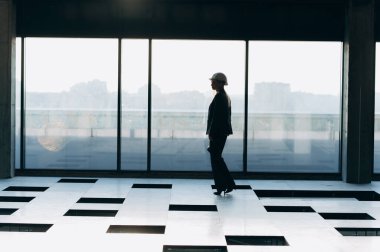 Beyaz miğferli bir kızın silüeti panoramik pencerenin yanında yürüyor..