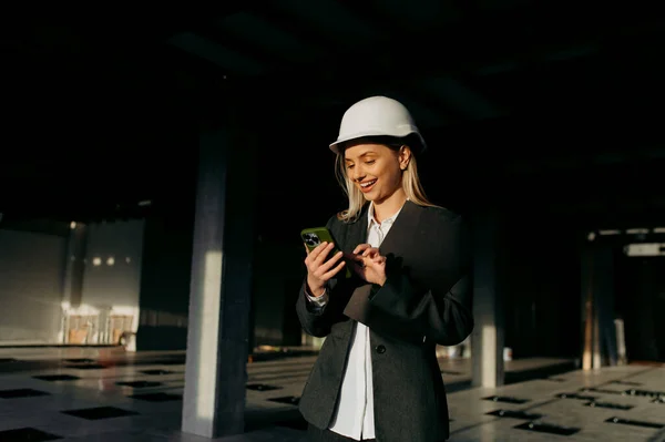 若い建築家の女性がオフィスでスマートフォンを使って笑顔で幸せ — ストック写真