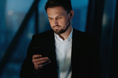 İşadamı gece ofiste akıllı telefon kullanır..