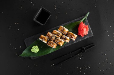 Siyah arka planda yılan balığı, susam ve Philadelphia peynirli suşi rulosu. Japon yemeği..