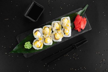 Krem peynirli suşi, pilav, sos. Maki suşisi siyah bir arkaplanda yuvarlanıyor..