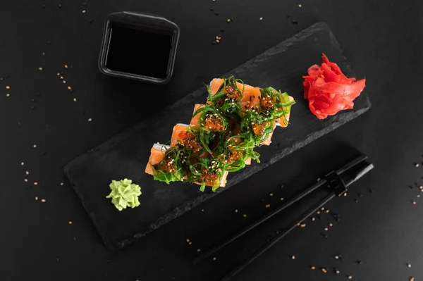 Kırmızı balıklı suşi, havyar, yosun, peynir ve siyah arka planda kivi..