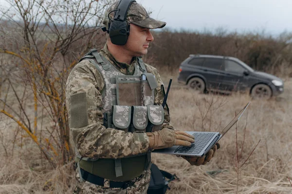 military man stands in camouflage and works with a laptop.