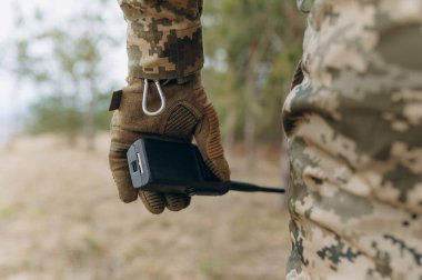 Kamuflaj üniforması ve taktik eldiven giymiş bir asker telsiz tutuyor. Ukrayna ordusunun savaş sırasındaki iletişimi.