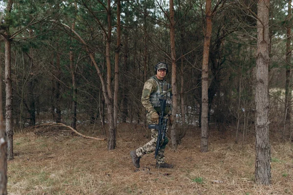 a soldier walks through the forest with a machine gun.
