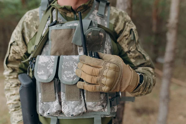 stock image a military man in a camouflage uniform and tactical gloves holds a walkie-talkie. communication of the Ukrainian army during the war.
