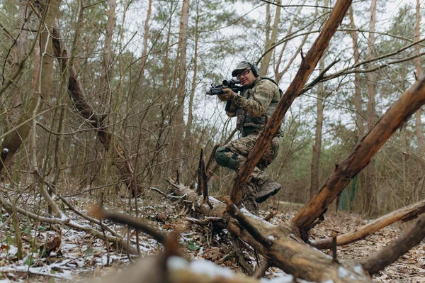 military man in camouflage uniform on tree branches, in an ambush with a weapon, a machine gun. military actions a soldier in the forest.