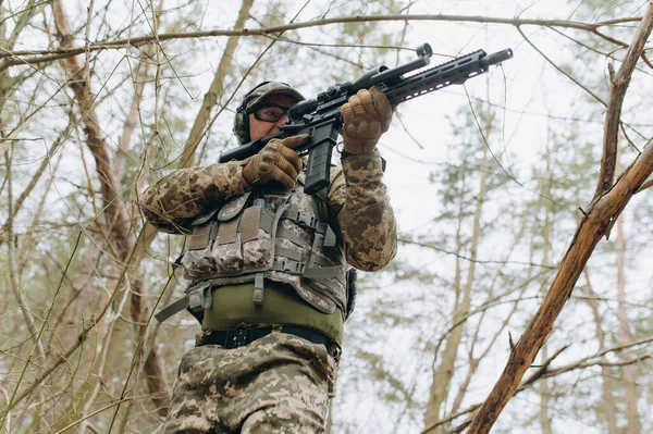 military man in camouflage uniform on tree branches, in an ambush with a weapon, a machine gun. military actions a soldier in the forest.