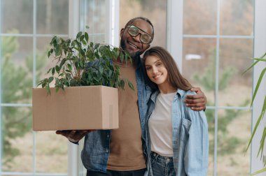 Genç ve mutlu bir aile bir eve taşınıyor. Siyahi bir adam ve kadın hareket etmek ve gülümsemek için karton kutular tutuyorlar. taşınan kutular
