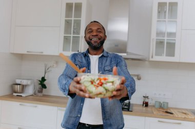 Afro-Amerikalı bir adam mutfakta salata tutuyor..