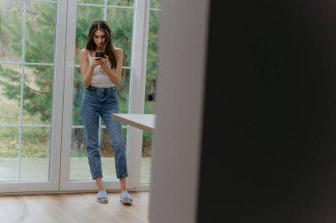 Kız cep telefonunda internette geziniyor, sohbet ediyor, mesajları okuyor, sanal gülümseme kullanıyor.