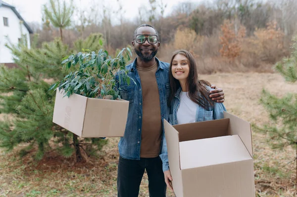 A happy young family is moving into a house. A black man and woman are holding cardboard boxes for moving, smiling. moving boxes