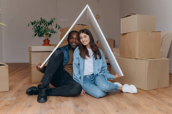 a couple moves into their own house, together they make a gesture of the roof of the house, sit on the floor among cardboard boxes