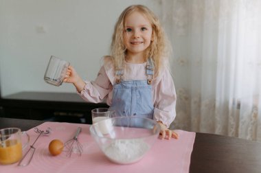 Pişirme malzemeleri olan küçük bir kız. Çocuk yemek ve kurabiye hazırlıyor. Çocuk eğleniyor, yemek yapmayı ve mutfakta oynamayı öğreniyor..