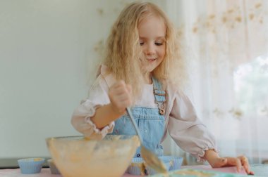 Küçük kız mutfakta kurabiye pişiriyor, dilini gösteriyor.