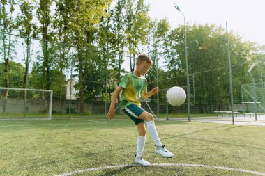 Çocuk futbol sahasında topla oynuyor.