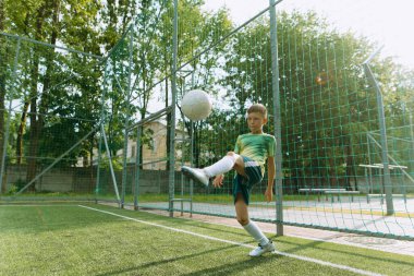 Çocuk futbol sahasında topla oynuyor.