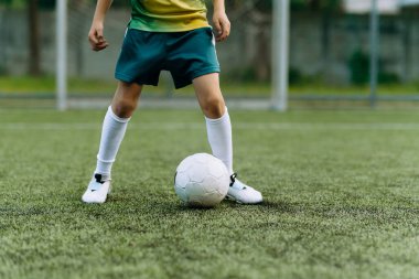 Yeşil üniformalı bir futbolcu çocuk futbol sahasında topla koşuyor.
