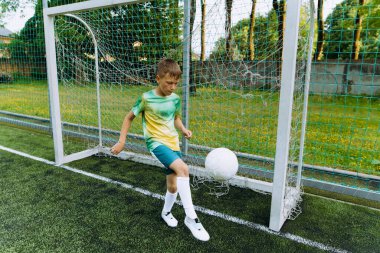 Çocuk futbol sahasında topla oynuyor.