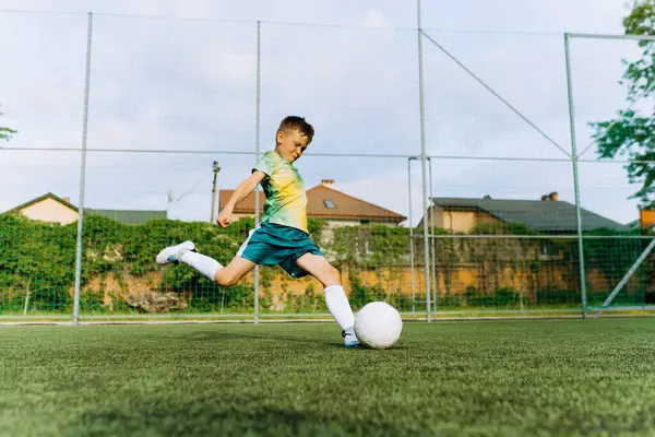 a small football player kicks the ball at the goal. Boy Playing Soccer Game