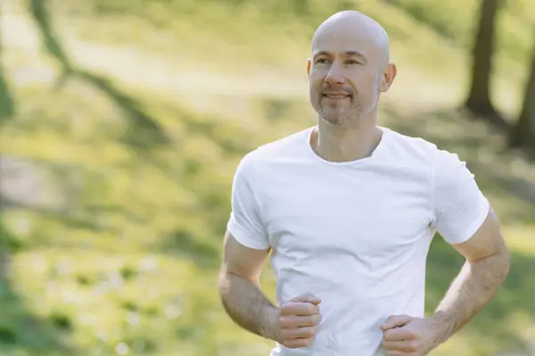 Genç adam güneşli bir yaz gününde kulaklıkla parkta koşuyor.