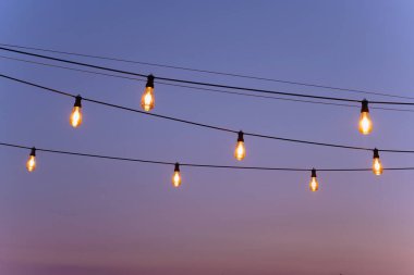 Sarı ampullerin şenlikli dekoru. Akşam yemeği partisinde bir dizi ışık parlıyor. Kabloda bir sırada ampuller