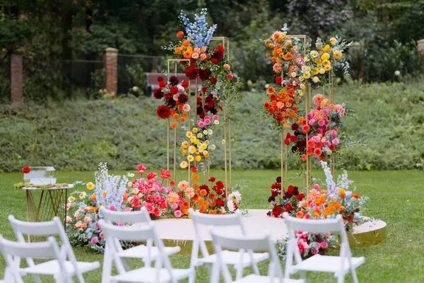 Düğün kemeri açık havada parlak çiçeklerle süslenmiş. Bahçedeki yeşil çimenlikte düğün töreni.