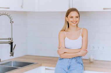 Genç, güzel, modern bir kadın mutfaktaki masanın yanında duruyor. Mutfakta gülümseyen genç bir kızın portresi.