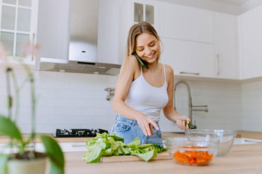 Genç, güzel bir kız mutfakta vitamin salatası yapıyor ve telefonda konuşuyor. Sağlıklı Yeme