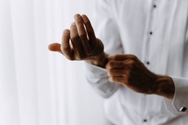 Beyaz gömlek giyen bir adam var. Kolları ve düğmeleri ayarlıyor. Adam bir erkek gömleği giyer, resmiyet kavramı ve detaylara dikkat eder.