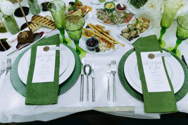 Düğün ziyafeti. Konuklar için yeşil dekorlu masa, çatal bıçak takımı, yeşil çiçekler ve beyaz masa örtüsüyle kaplı tabaklar. yeşil dekor