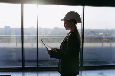Güzel bayan mühendis, tasarımcı, ofiste koruyucu beyaz kasklı bir mimar. İnşaat konsepti, ofis tasarımı. Güzel bayan mühendis koruyucu beyaz kaskla ofiste..