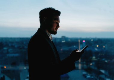 İşadamı gece ofiste akıllı telefon kullanır. Adam akşamları ofiste telefonda çalışıyor..