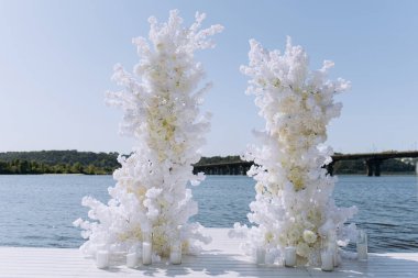 Şehrin nehir kenarına beyaz gül çiçekleriyle süslenmiş güzel bir düğün kemeri. Güneşli yaz gününde düğün töreni. beyaz düğün kemeri