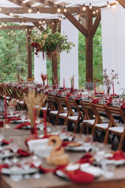 A large, long, decorated, wooden table and chairs, with dishes, flowers, candles. Pavilion in the forest in nature. Wedding banquet. banquet in nature