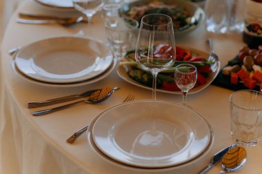Beyaz tabaklar ve cam eşyalar içeren güzel bir yemek düzeni. Taze sebzeler ve aperatifler davetkar bir şekilde servis edilmeye hazır..