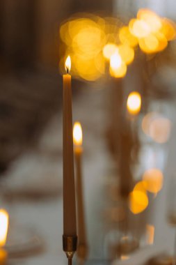 Yumuşak, parıldayan ışıkların arkaplanına odaklanmış yanan bir mum. Sahne sükuneti somutlaştırıyor, özel parıltısıyla yemek deneyimini güçlendiriyor..