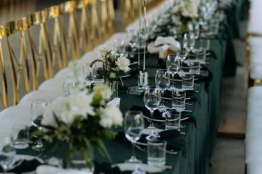 Sofistike masa düzenlemesi. Parlak cam süslemelerin yanında beyaz çiçekler sergileniyor. Titizlikle hazırlanmış bir yemek salonunda kaliteli bir etkinlik için koyu renk çarşaflar ve ince çatal bıçak bulunur..