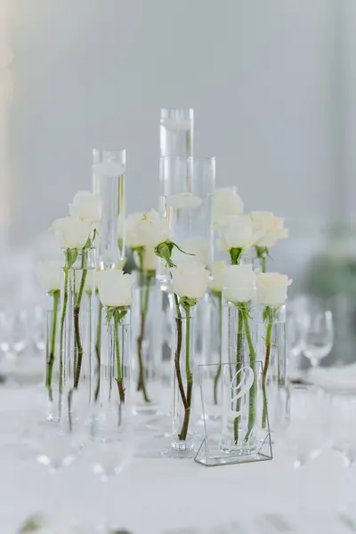 Cam vazolarda beyaz güller, kaliteli porselenler ve çatal bıçaklarla dolu güzel bir masa. Düğün için mükemmel bir ortam. Ya da şık bir ortam için..