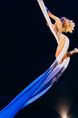 Bir akeralist büyüleyici bir performans sırasında kumaşla zarif bir şekilde etkileşime girer. Sanatçı, karanlık sahne arkaplanına karşı güç ve zarafet sergiliyor.