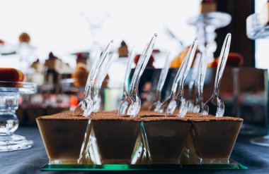 Çikolatalı mus fincanları şık kaşıkların yanına dizilmiş. Arkaplan, sunumu geliştirerek tatlıların çekici bir çeşidini gösteriyor.