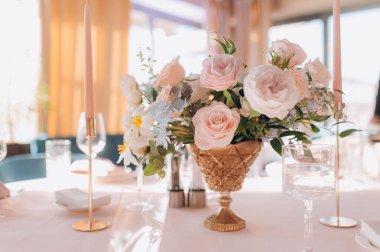 Pembe güllerle çiçek aranjmanı sunan şık bir tablo. Diğer elementler arasında uzun mumlar da var. Düğün masası dekorasyonu