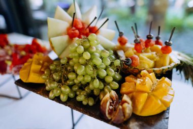 Tahtaya ustalıkla dizilmiş canlı taze meyve çeşitleri. Sergide üzümler, mangolar ve dilimlenmiş kavunlar yer alıyor..