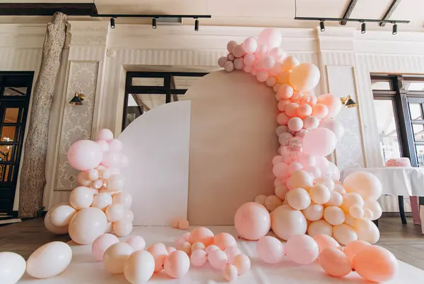 Büyüleyici bir pastel balon kemeri olay atmosferini güçlendirir. Düzenleme yumuşak pembe ve şeftali tonlarını içeriyor..
